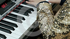 Teen girl in a shiny golden blouse plays the electric piano. Children`s fingers press the keys of the synthesizer