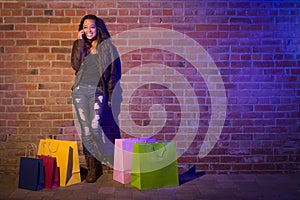 Teen Girl with Shopping Bags Using Cell Phone Against Brick Wall