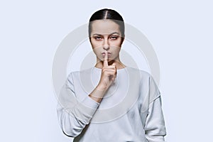 Teen girl showing silent gesture with finger on lips, white background