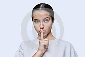 Teen girl showing silent gesture with finger on lips, white background