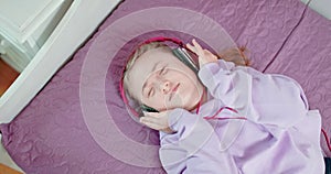 Teen girl is singing with closed eyes lying on her bed in bedroom wearing headphones