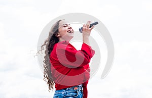 teen girl singing song in microphone on sky background, music