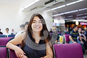 Teen girl sitting at airport departure lounge, smiling