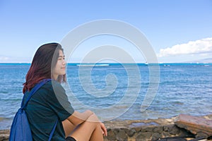 Teen girl sitting alone along ocean shore resting