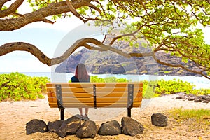 Teen girl sitting on bench under trees by ocean