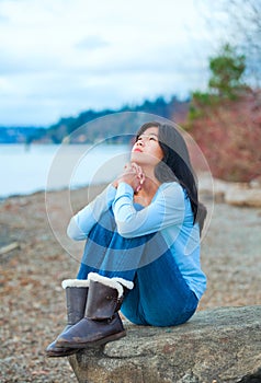 Teen girl sitting on boulder along lake shore praying