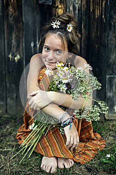 A teen girl is sitting with a bouquet of daisies.