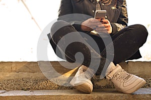 Teen girl sitting on concrete steps holding phone in hands. Teenager. Hipster. Communication. On open air. Close-up. Cropped photo