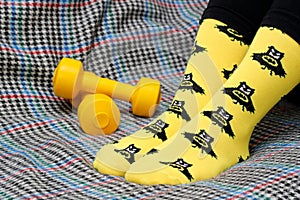 Teen girl sitting on couch. Yellow socks with black Batman pattern. Dumbbells. Side view