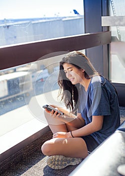 Teen girl sitting on floor at airport looking at smartphone