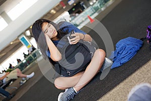 Teen girl sitting on floor at airport looking at smartphone