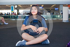 Teen girl sitting on floor at airport terminal holding luggage