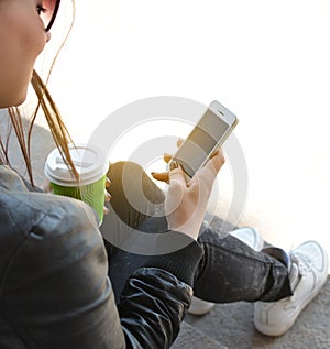 Teen girl sitting with mobile phone and coffee in hands, on concrete ancient stone floors. Teenager. Hipster. Communication. On