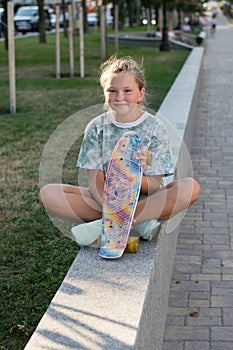 Teen girl sitting in the park with a skateboard in his hand. Leisure of teenagers without gadgets