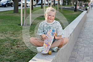 Teen girl sitting in the park with a skateboard in his hand. Leisure of teenagers without gadgets