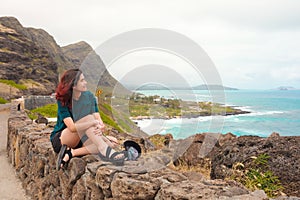 Teen girl sitting on rock wall overlooking Hawaiian ocean