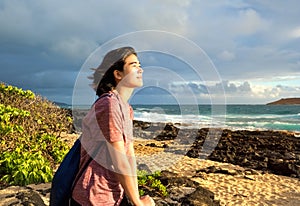 Teen girl sitting on rocky beach watching the hawaiian sunrise