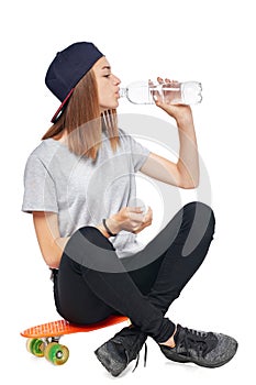 Teen girl sitting on skate board drinking water