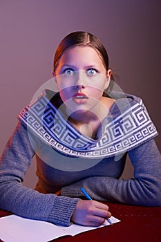 Teen girl sitting at table with pen in her hand