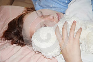 Teen girl sleeping in an embrace with a white teddy bear in bed