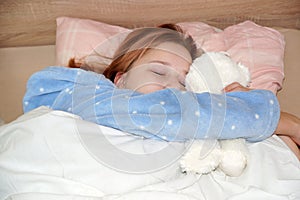 Teen girl sleeping in an embrace with a white teddy bear in bed