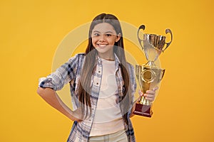 teen girl smile and hold her award champion cup isolated on yellow. teen girl receive award in studio. teen girl accept