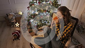 Teen girl smiling and drinking tea from a cup. Christmas tree and holidays mood. 4K UHD.