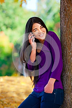 Teen girl standing against autumn tree talking on cell phone