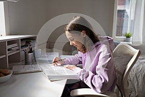 Teen girl studying alone reading textbook sitting at home desk