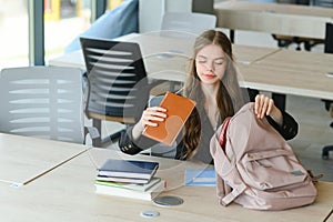 Teen girl studying with textbook writing essay learning in classroom.