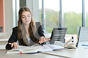 Teen girl studying with textbook writing essay learning in classroom.