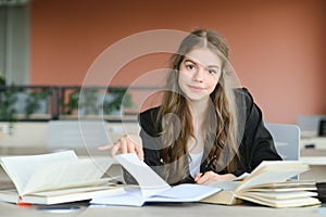 Teen girl studying with textbook writing essay learning in classroom.