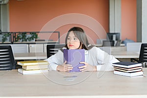 Teen girl studying with textbook writing essay learning in classroom.