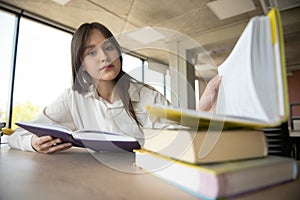 Teen girl studying with textbook writing essay learning in classroom.