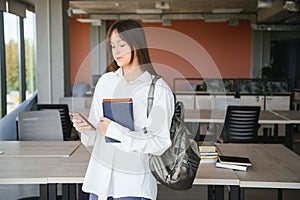 Teen girl studying with textbook writing essay learning in classroom.