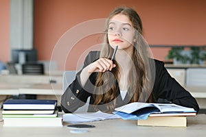 Teen girl studying with textbook writing essay learning in classroom.