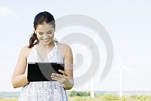 Teen girl with tablet computer next to wind turbine.