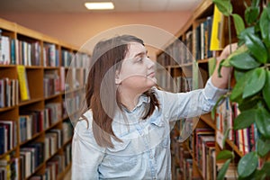 Teen girl taking   book from bookshelves in library, choosing