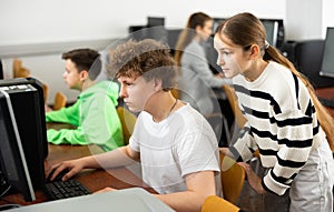 Teen girl talking to concentrated teenager studying in computer lab