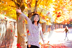 Teen girl throwing colorful autumn leaves in air under trees