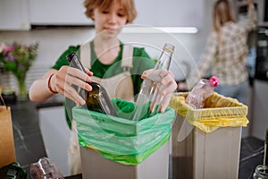 Teen girl throwing glass bottles in recycling bin in the kitchen.