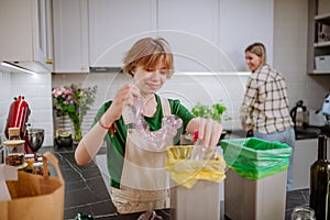 Teen girl throwing plastic bottles in recycling bin in the kitchen.