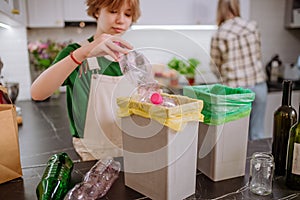 Teen girl throwing plastic bottles in recycling bin in the kitchen.