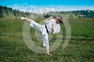 Teen girl training karate kata outdoors, performs the yoko geri kick