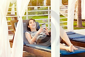 Teen girl using smartphone while relaxing on lounger at resort