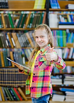 Teen girl using a tablet computer in a library and showing thumbs up