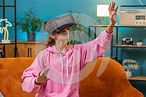 Teen girl using virtual reality futuristic technology headset to play simulation 3D video game home