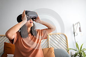 Teen girl using VR headset at home. Amazed Asian young female wearing virtual reality goggles.