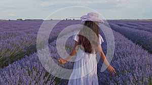 Teen girl walks by blooming lavender fields with blue lavender flowers.