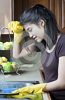 Teen girl washing dishes at kitchen sink, tired